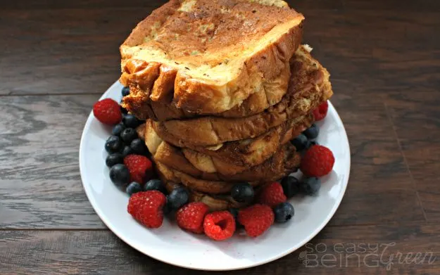 french toast stacked on white plate with berries around on brown wood background