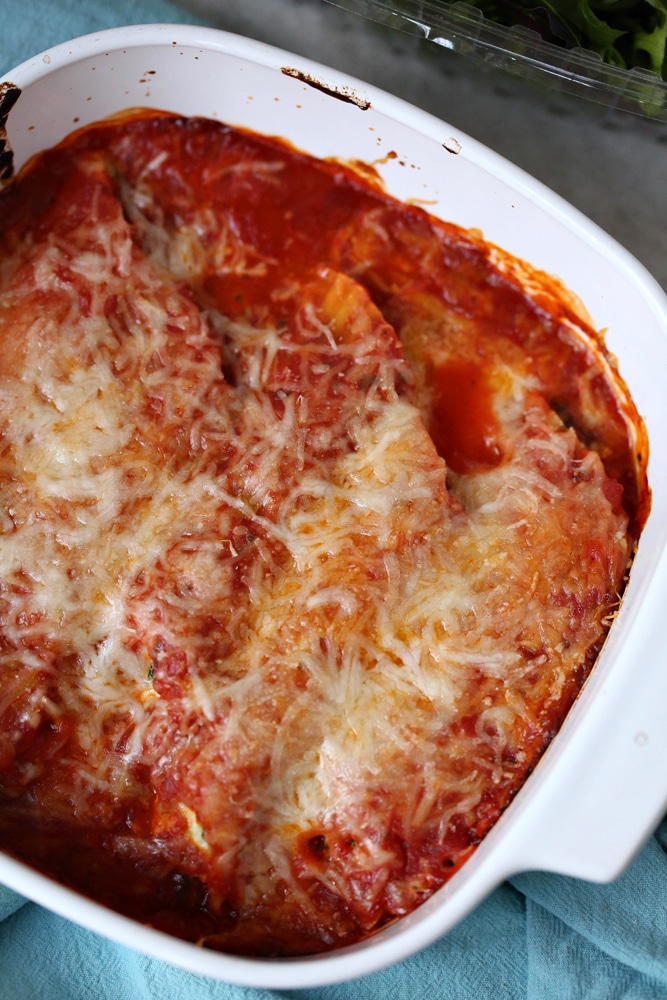 cheese and marinara sauce over manicotti noodles in white dish