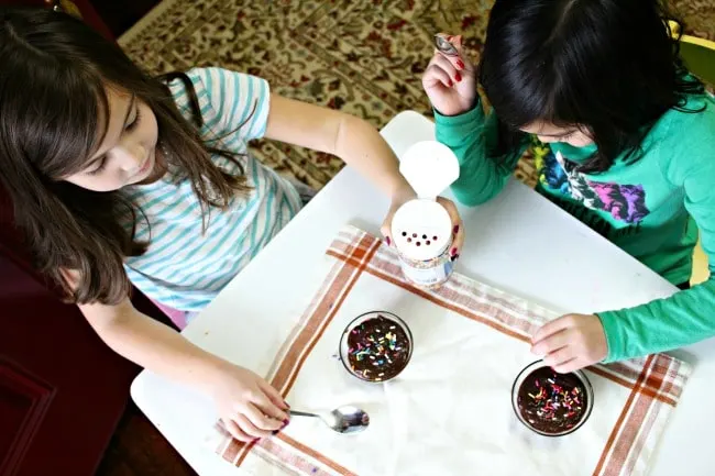 Two girls adding sprinkles to almond milk chocolate pudding
