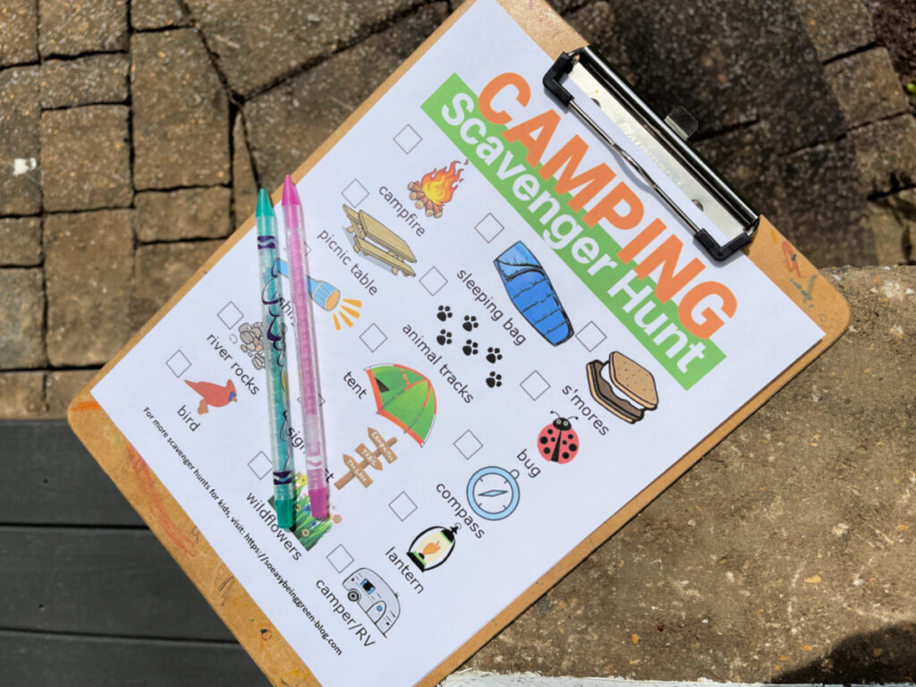 camping scavenger hunt printable on clipboard with crayons sitting on rock stones